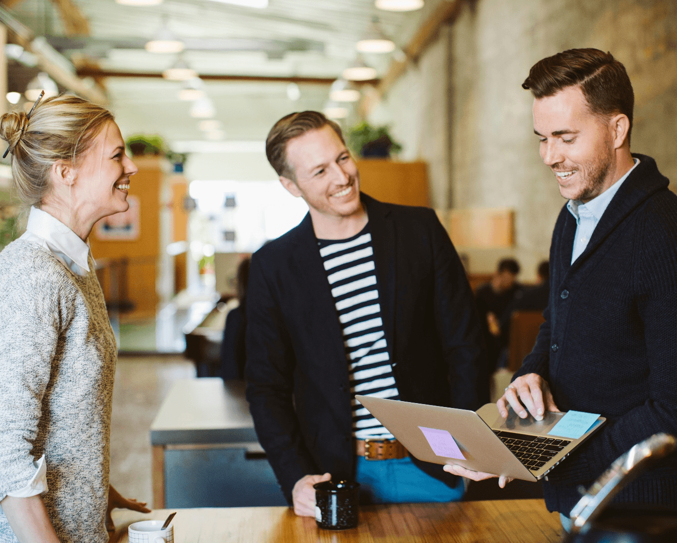 Three colleagues laughing over a laptop in an open-plan office